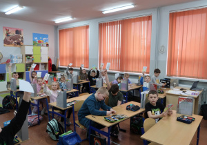 Uczniowie w sali klasowej kolorują laurki.